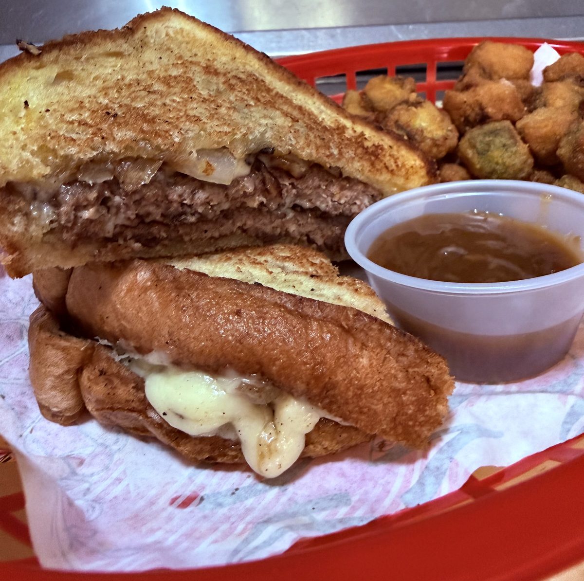 French dip burger on Texas toast with melted cheese, a cup of dipping gravy and fried okra